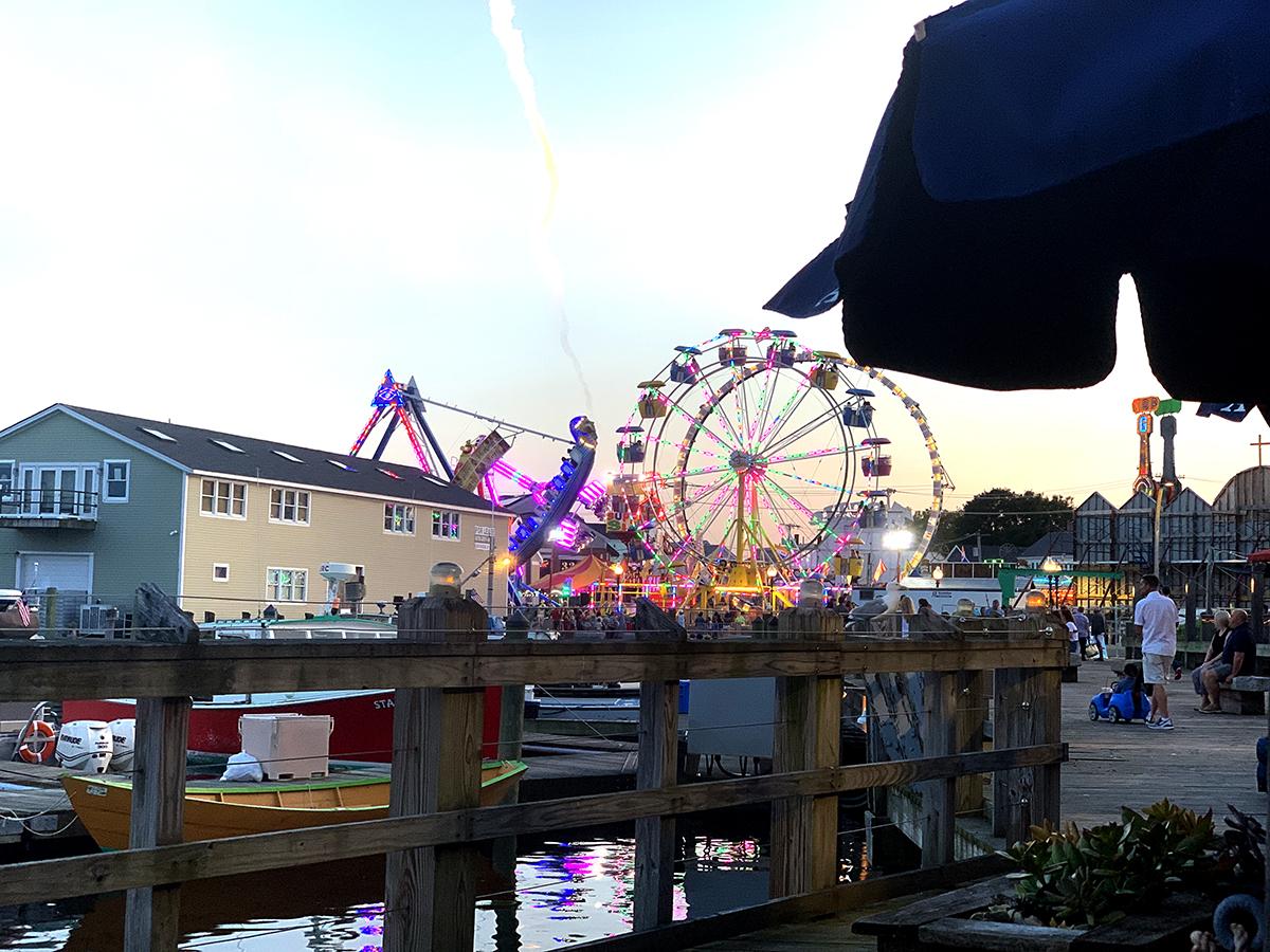 Carnival at dusk with a Ferris wheel and colorful lights by the waterfront.