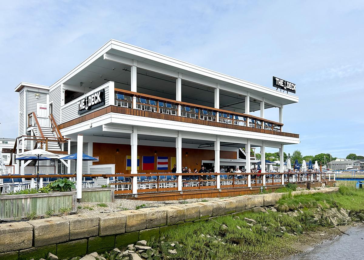 Two-story building with balconies and outdoor seating by a grassy area.