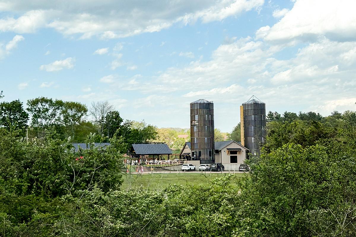 Farm silos and buildings surrounded by trees under a partly cloudy sky.
