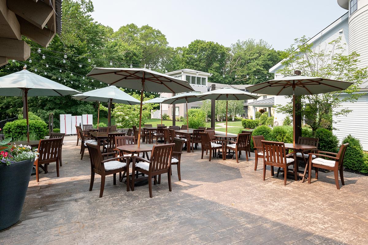Outdoor patio with tables, chairs, and umbrellas, surrounded by greenery.