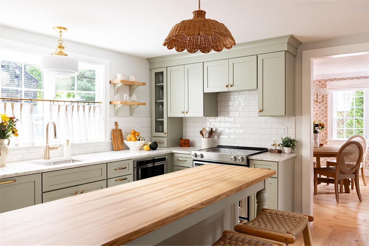 Bright kitchen with light green cabinets, wooden island, and wicker pendant light.