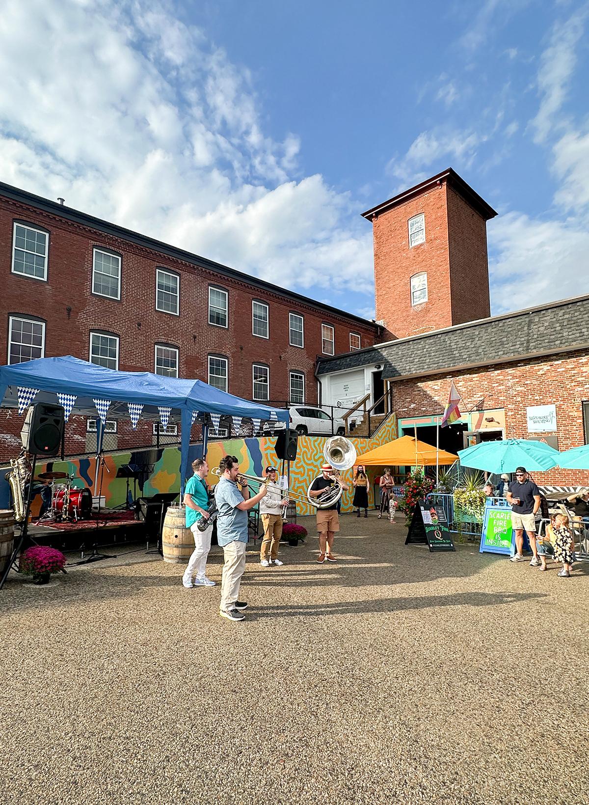 Outdoor market with colorful stalls beside red brick buildings under a blue sky.