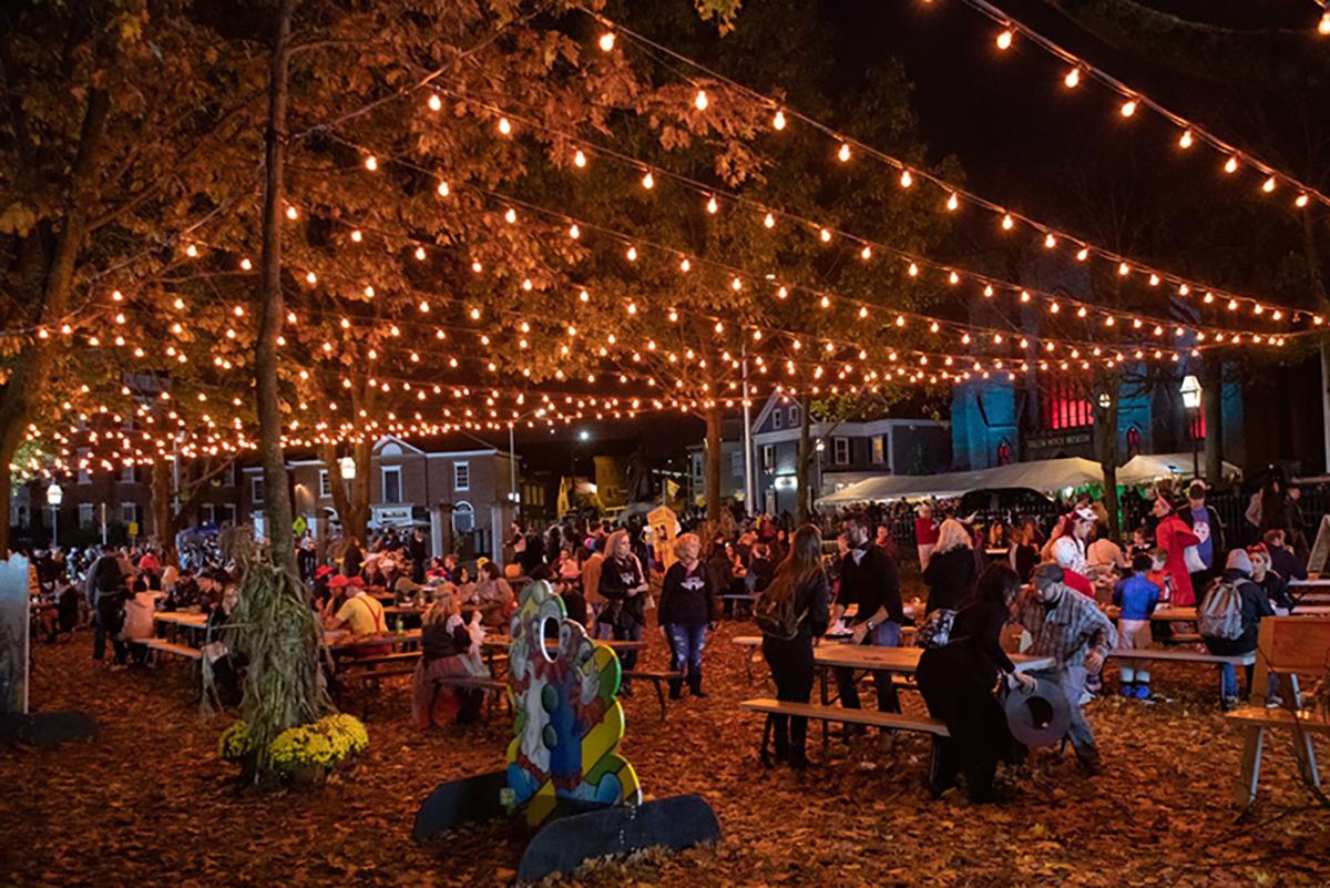 Outdoor evening festival with string lights, food stalls, and people at picnic tables