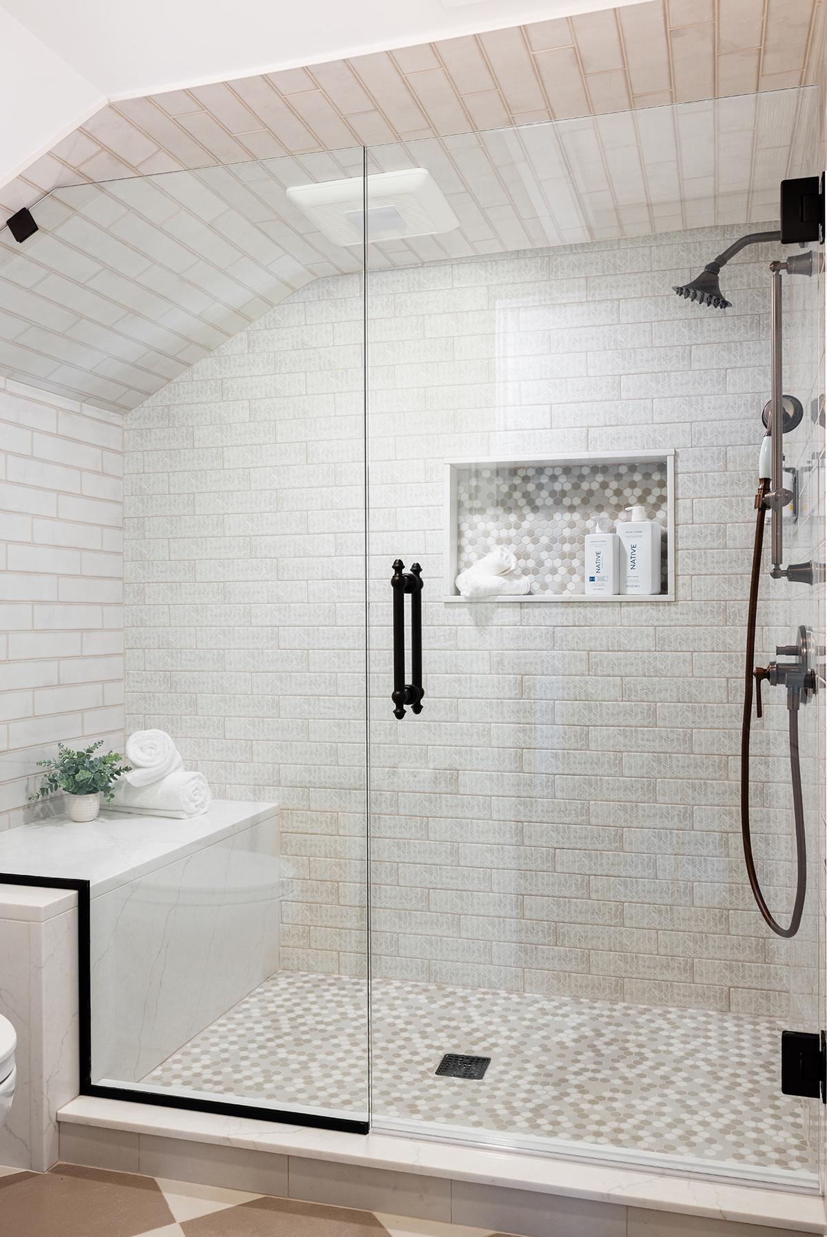 Modern walk-in shower with glass door, white tile, and black fixtures