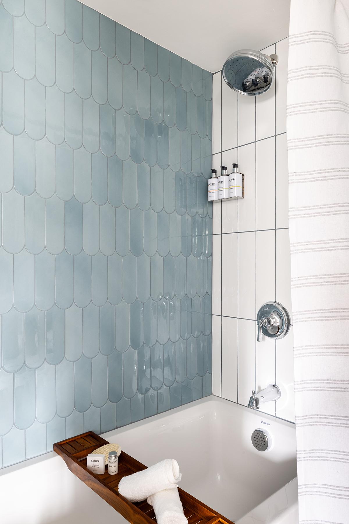 White tiled shower with blue glass wall, chrome fixtures, and bathtub tray.