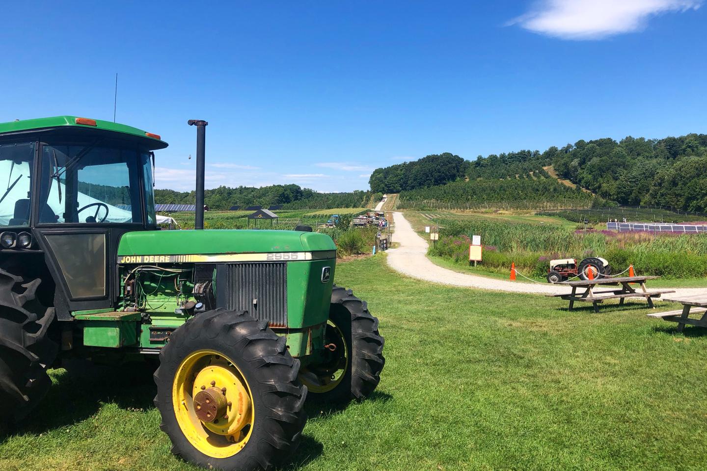 Green tractor beside a rural road and picnic table under a blue sky.