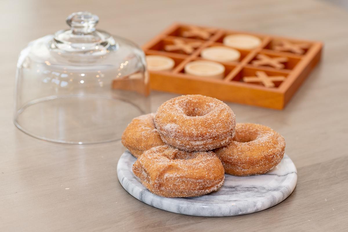 Sugared doughnuts on a marble plate beside a glass cloche and pastries.