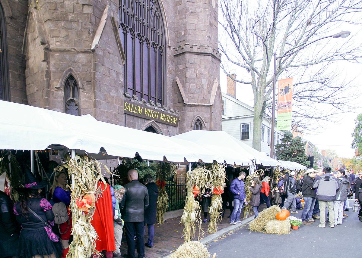 Outdoor market stalls beside a Gothic church, with shoppers and hanging clothing.