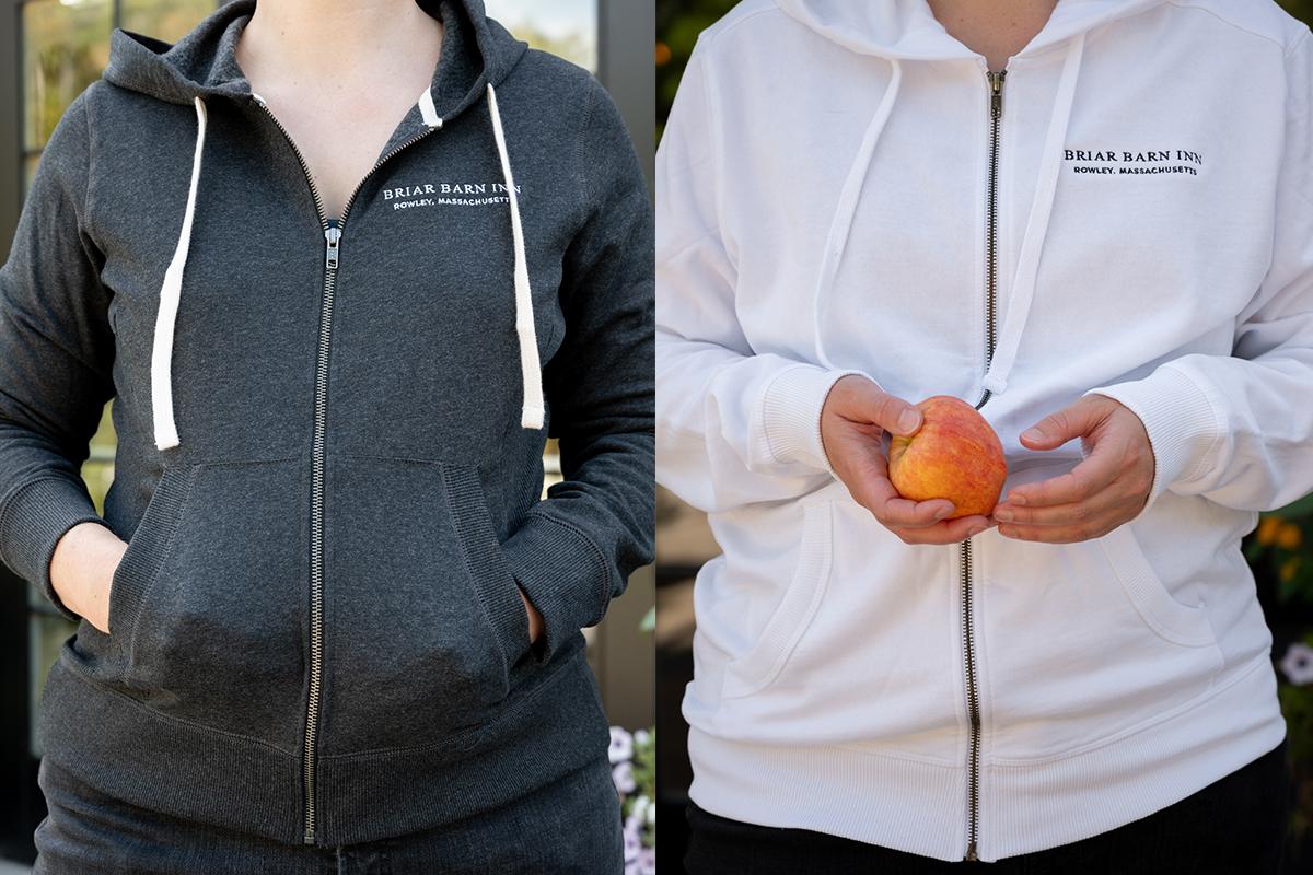 Two women wearing black and white zip-up hoodies, holding oranges.