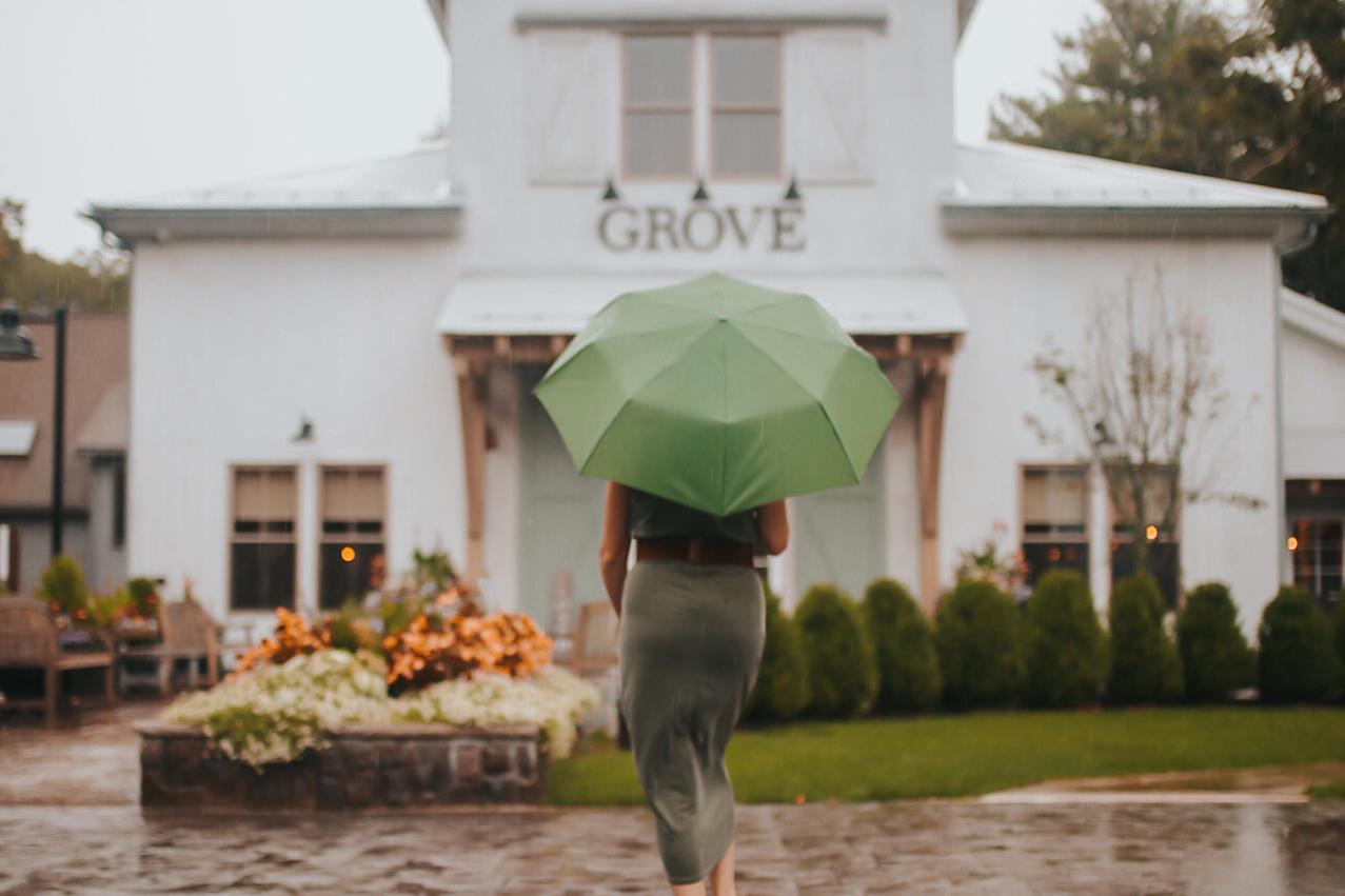 Person with a green umbrella walking toward Grove restaurant in the rain.
