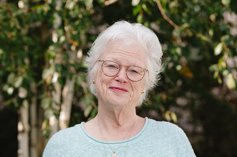Portrait of a smiling elderly woman with white hair and glasses outdoors.