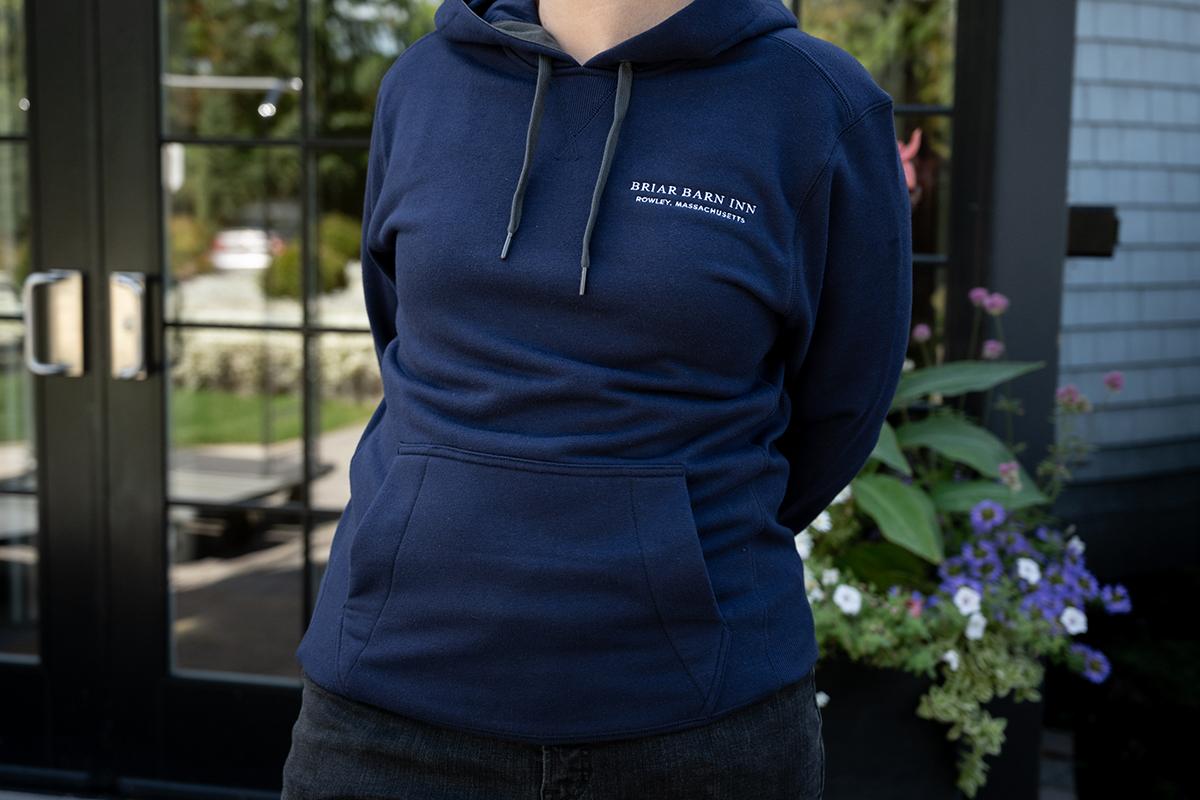Person in a navy hoodie standing outside a glass door beside purple flowers.
