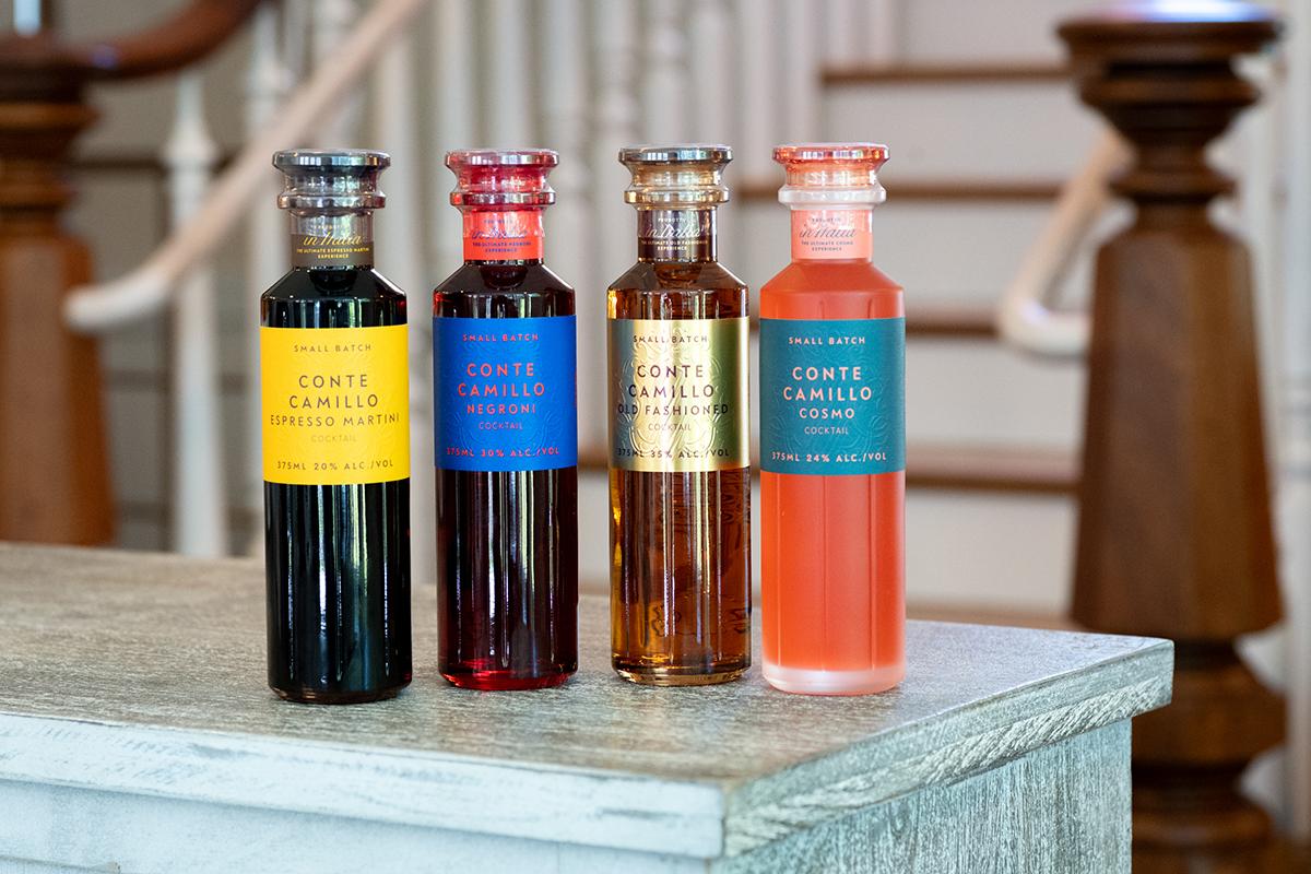 Four colorful bottled drinks on a rustic table beside wooden chairs.
