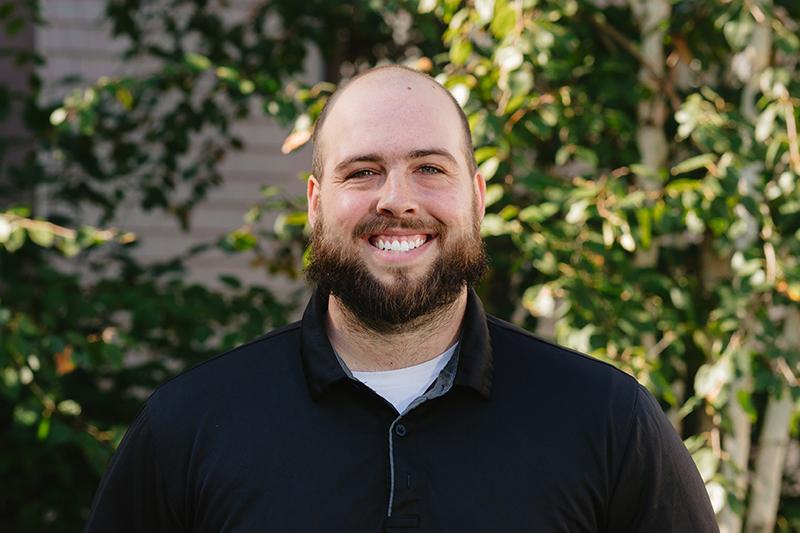 Smiling bald man with a beard in a black shirt outdoors.