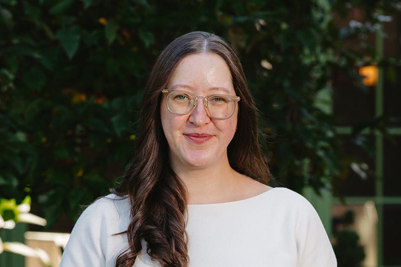 Portrait of a smiling woman with glasses in a white top outdoors.